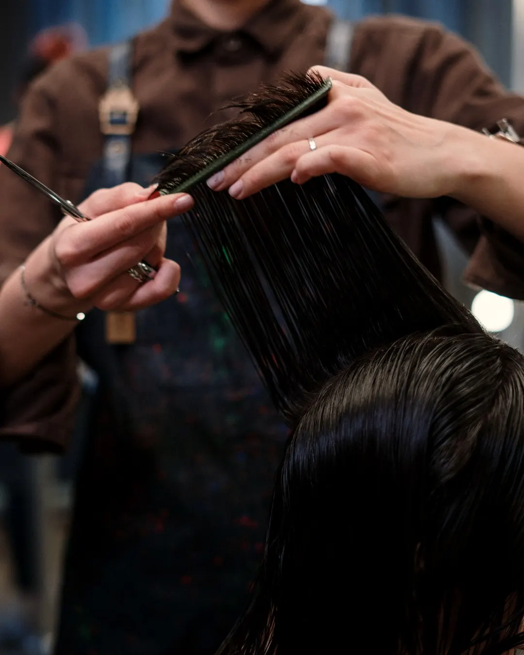 Un coiffeur coupe une mèche de cheveux bruns, peigne et ciseaux en main