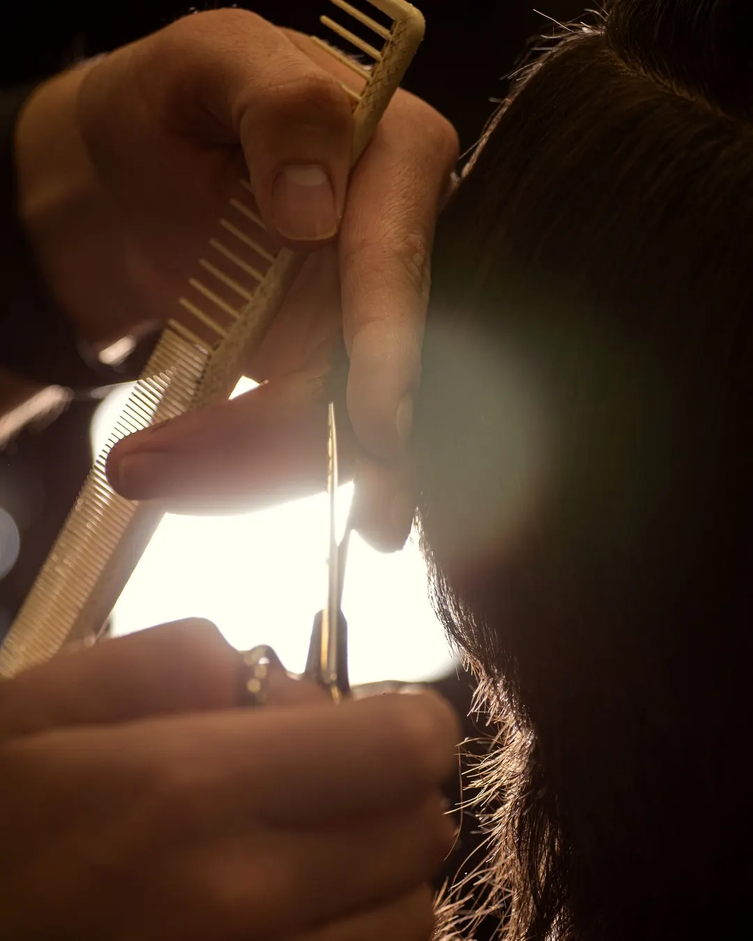 Mains d'un coiffeur tenant un peigne et des ciseaux, à contre-jour