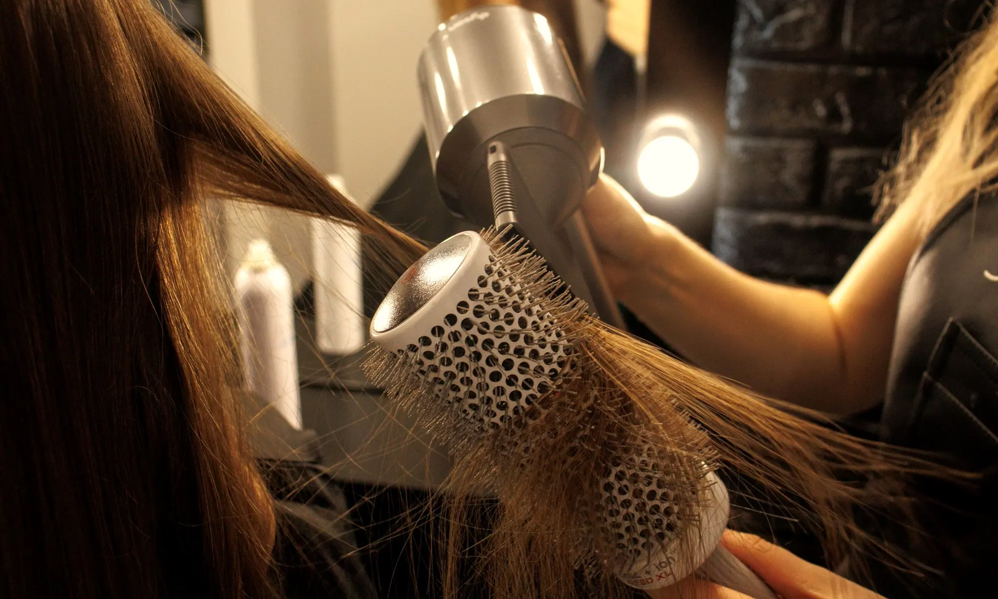 Brushing à la brosse ronde et au séchoir devant un miroir éclairé